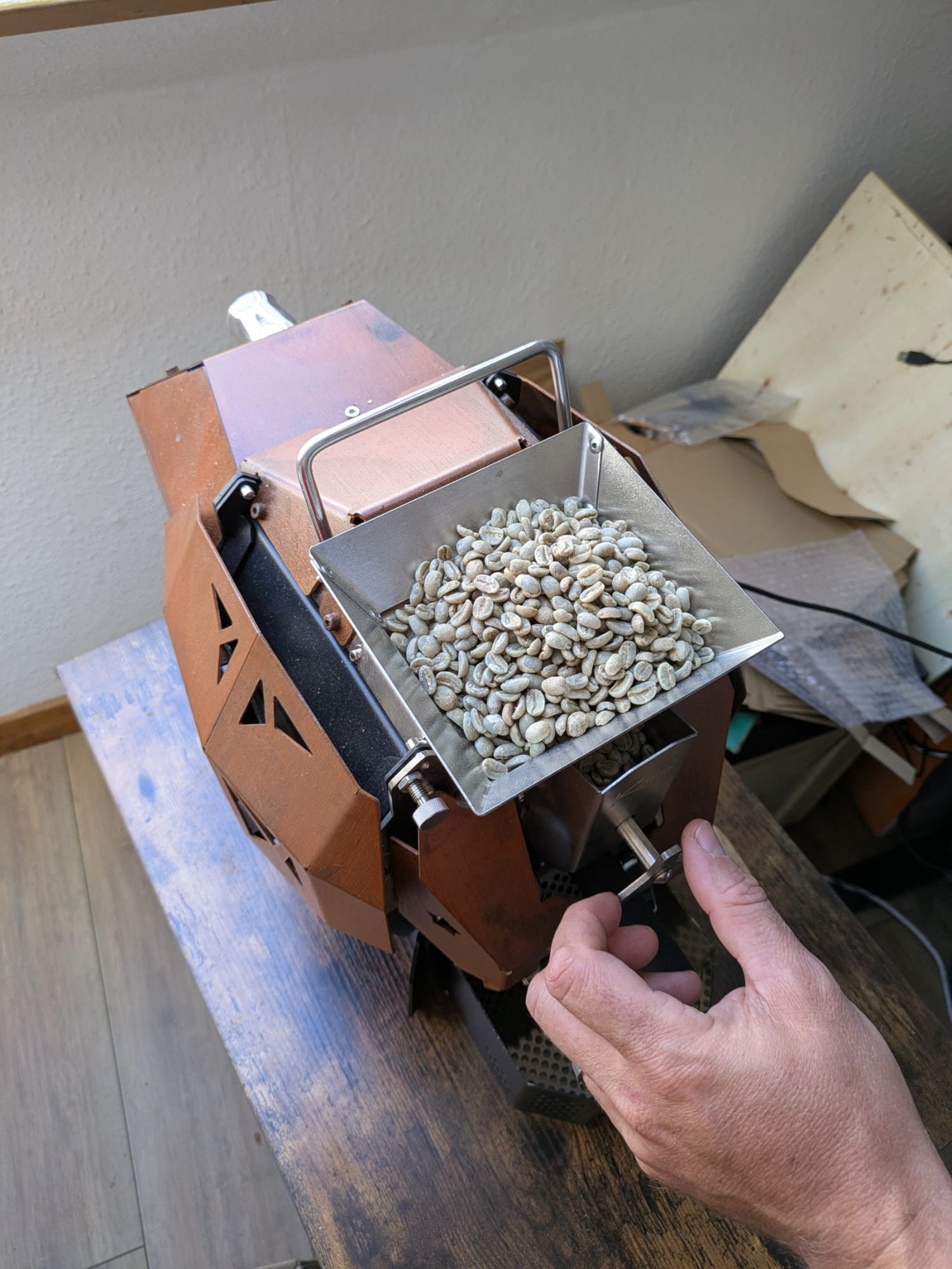 Hand holding a the dropper toto drop green coffee beans into the coffee roasting machine to start the roast