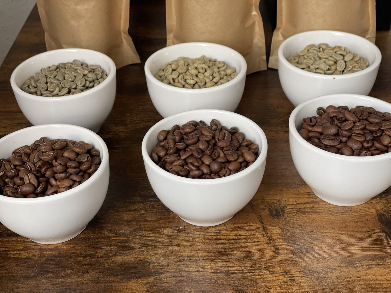 White bowls with coffee beans at different roast levels on a wooden surface